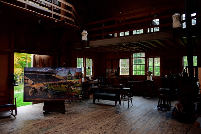 The inside of a studio with several northern windows, paintings, sculptures, and art supplies.