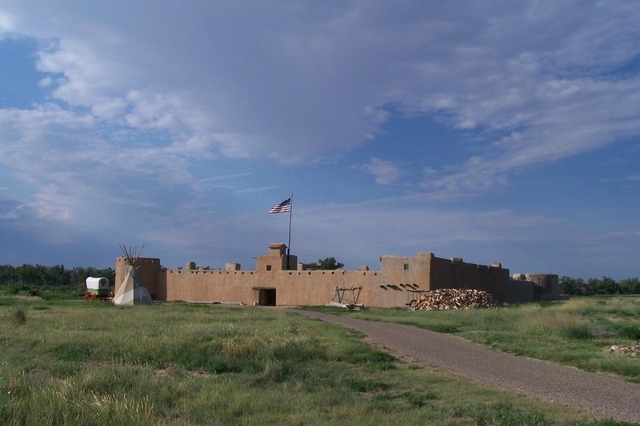 Bent's Old Fort with shortgrass prairie, tepee and wagon in foreground and blue sky & clouds above