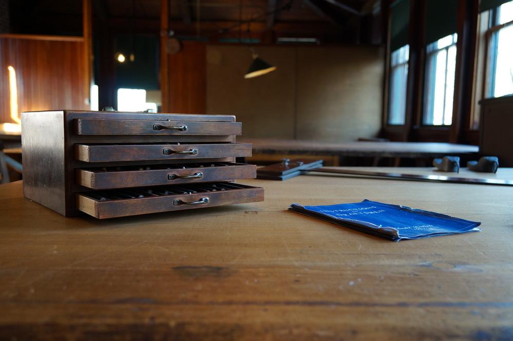 Dark wood box with four shallow drawers on large wooden table with blueprint