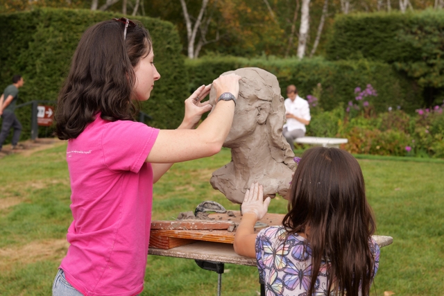 a child assists a sculptor with a clay bust