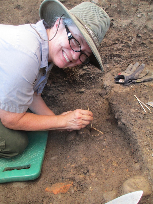 A woman digs in a carefully excavated hole.