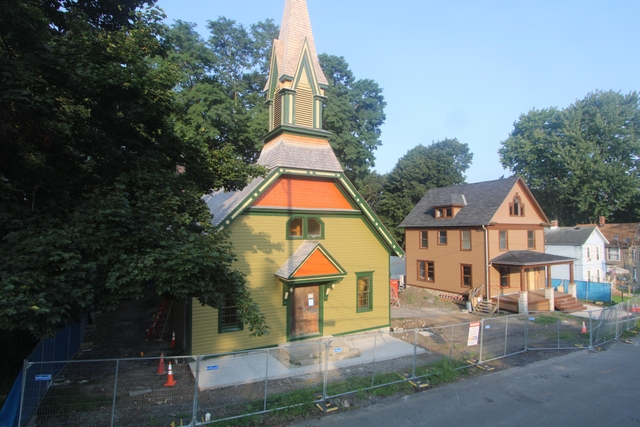 Wooden church with tall steeple, with construction equipment out front.