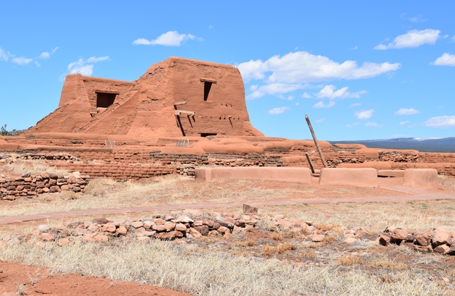 Large brown adobe mission church with low brick walls and kiva ladder in front