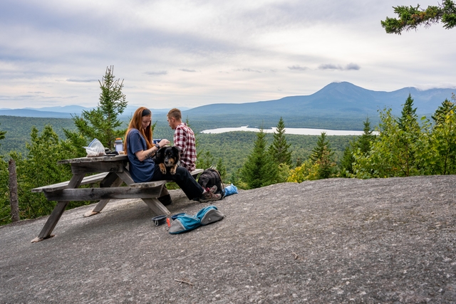 Hikers and a dog sit at a picnic table overlooking Katahdin.