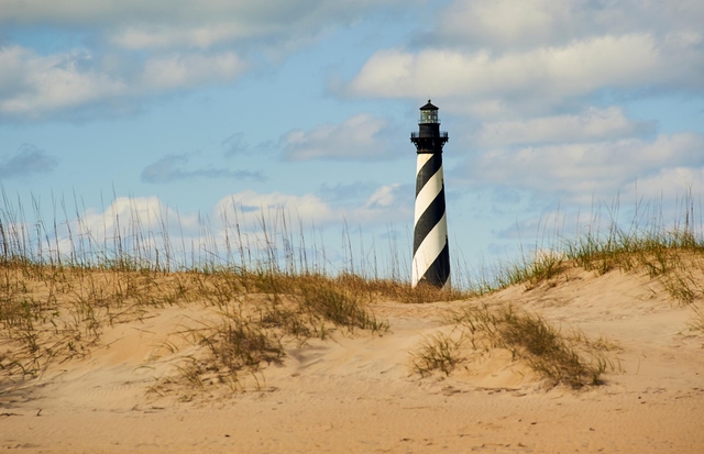 A beach landscape with the black and white spiraled lighthouse in the background