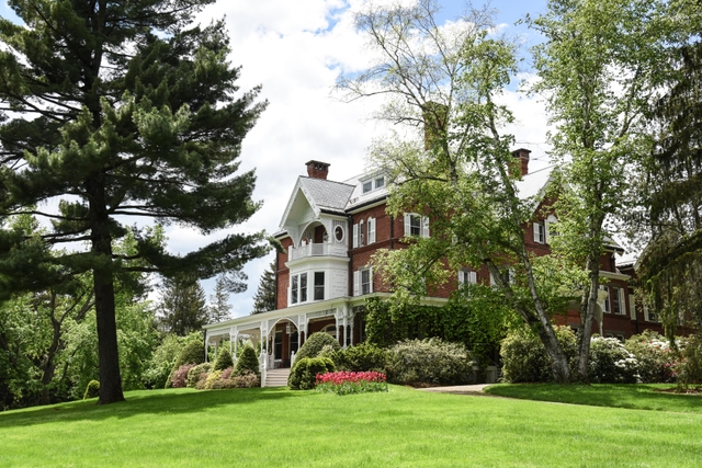 large red brick mansion with white lattice porch and lush green lawn