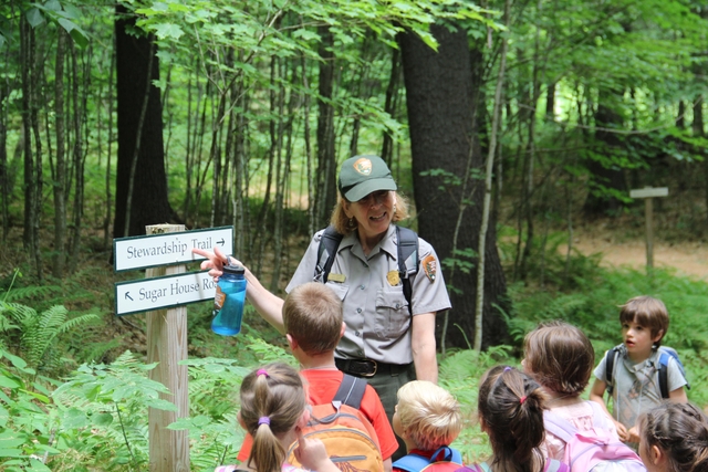 Park Ranger points to a trail sign and talks to a group of young children