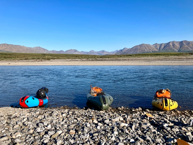 Three multicolored packrafts on the gravel shore of the Kelly river