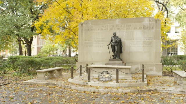 Bronze statue of George Washington standing over a tomb with an eternal flame .