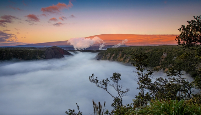 A cloud-filled volcanic crater at sunrise with a mountain rising behind