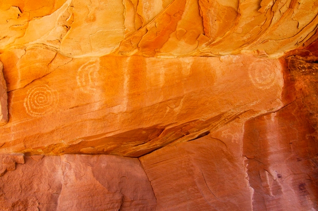 Reddish-orange sandstone wall with petroglyphs etched into it