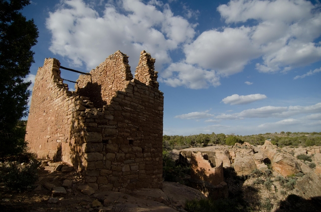 remains of a stone structure with wood beams on the edge of a canyon