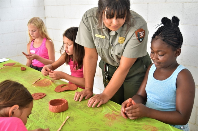 A woman standing next to a little girl helping her make a clay pot