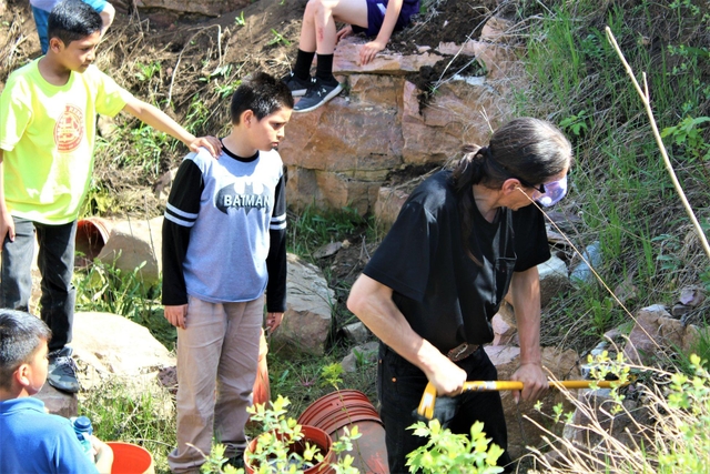 A man works with tools in a quarry as kids watch