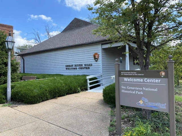 Blue building with a high pitched roof. A sign in front says, "Ste. Genevieve Welcome Center."