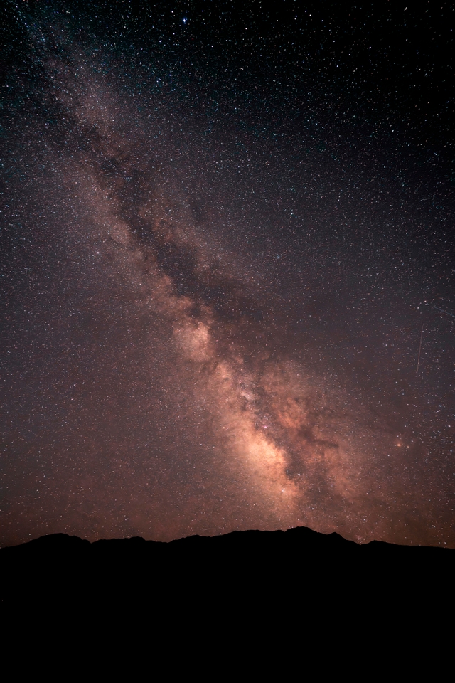 A dark, jagged mountain ridge runs along the bottom edge. Above it, a dense river of stars.