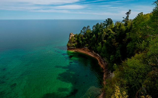 A sandstone rock formation rises out of a blue-green Lake Superior on a sunny day.