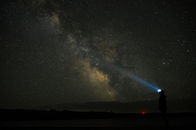 A person in a headlamp looks skyward at the milky way on a clear night