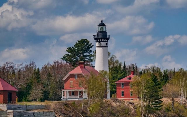 A white lighthouse tower surrounded by red brick buildings on a sunny day.