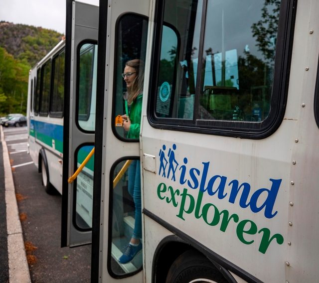 Woman steps out of the open double-doors of a white bus labeled Island Explorer.