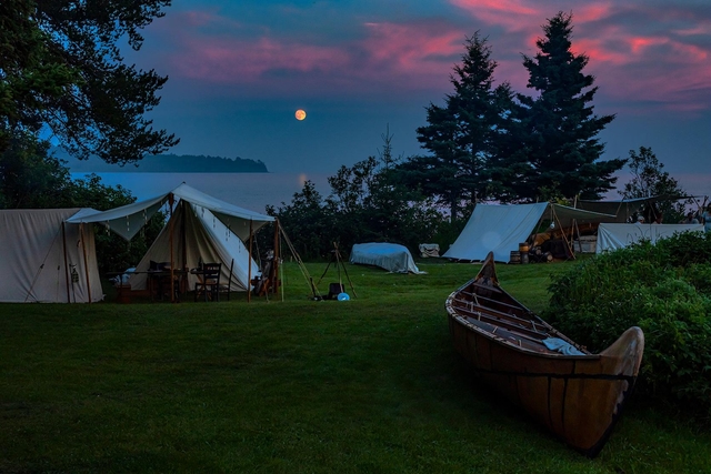 Moonrise over a lake with canvas tents in the foreground.