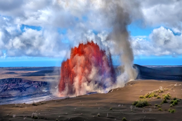 Fountains of molten lava erupting from within a crater next to a whirlwind formed from the eruption.