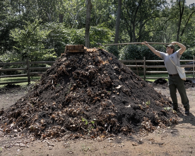 a large dirt pile with smoke coming out of the top. A park ranger scopes more dirt with a shovel.
